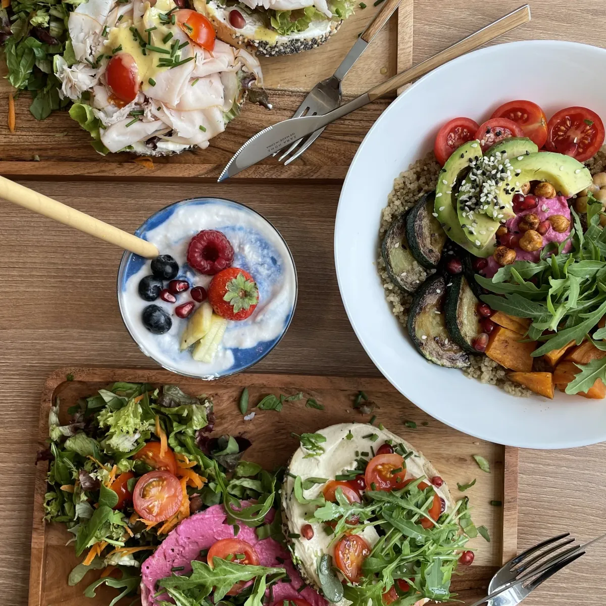 Von oben fotografiert: Bowl mit Quinoa, Avocado, Süßkartoffel und Rucola, daneben Toasts und ein Beeren-Joghurt