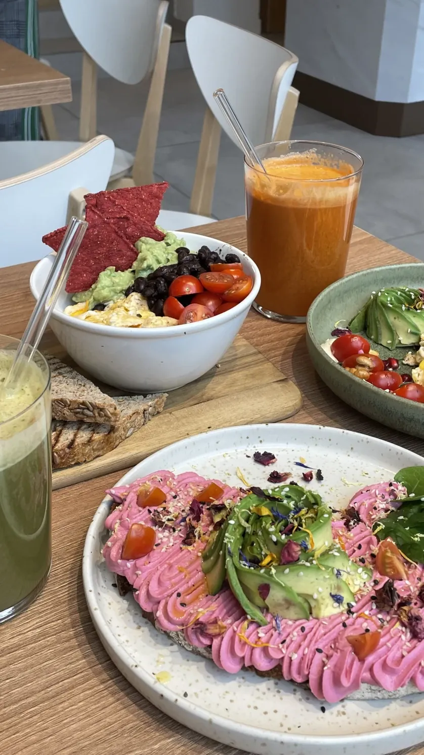 Toast mit pinker Rote-Bete-Creme, Avocadofächer, Kirschtomaten und Blütenblättern